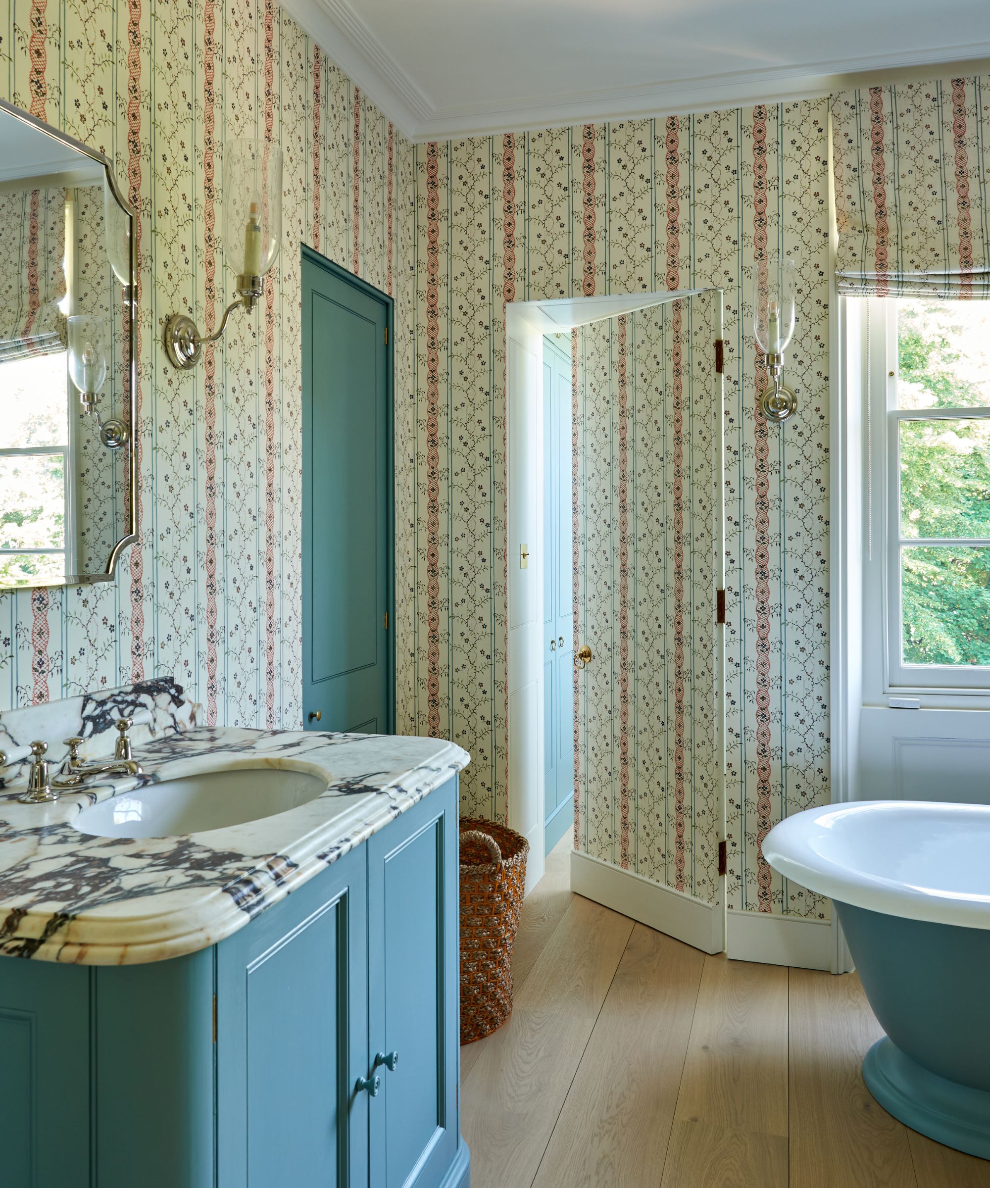 Vintage bathroom with striped wallpaper, blue bathtub and vanity with blue cupboard and marble sink