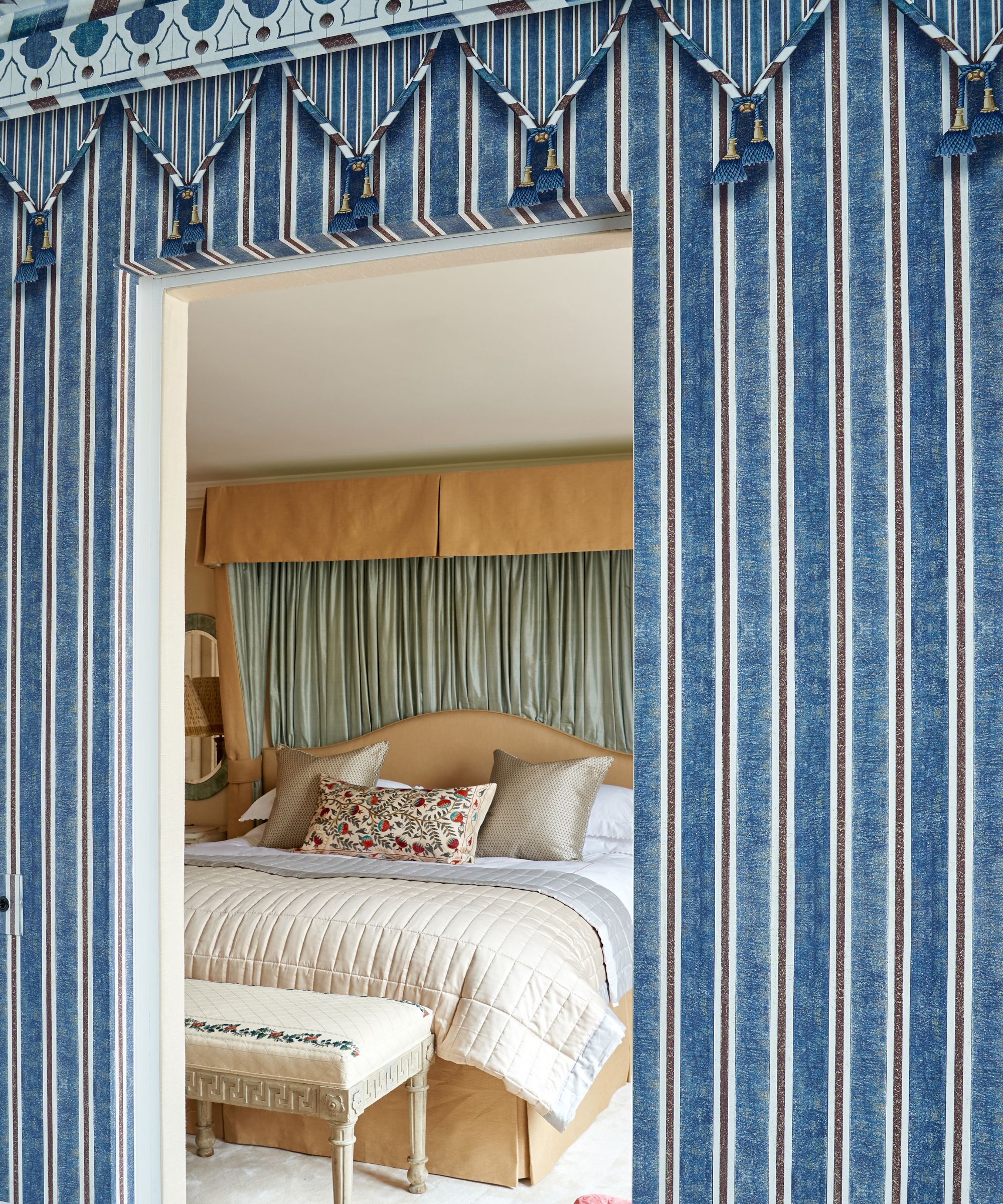 Stripe wallpaper doorway looking into bedroom with canopy, silk bedding and bench