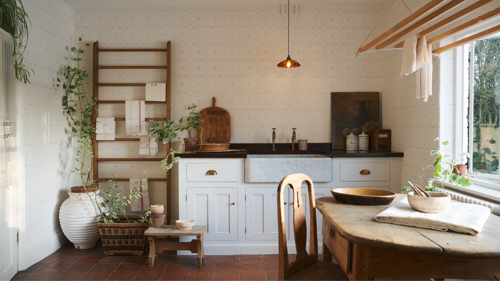 Farmhouse kitchen with wood round table, white cabinets, low pendant light, wood stall and plants