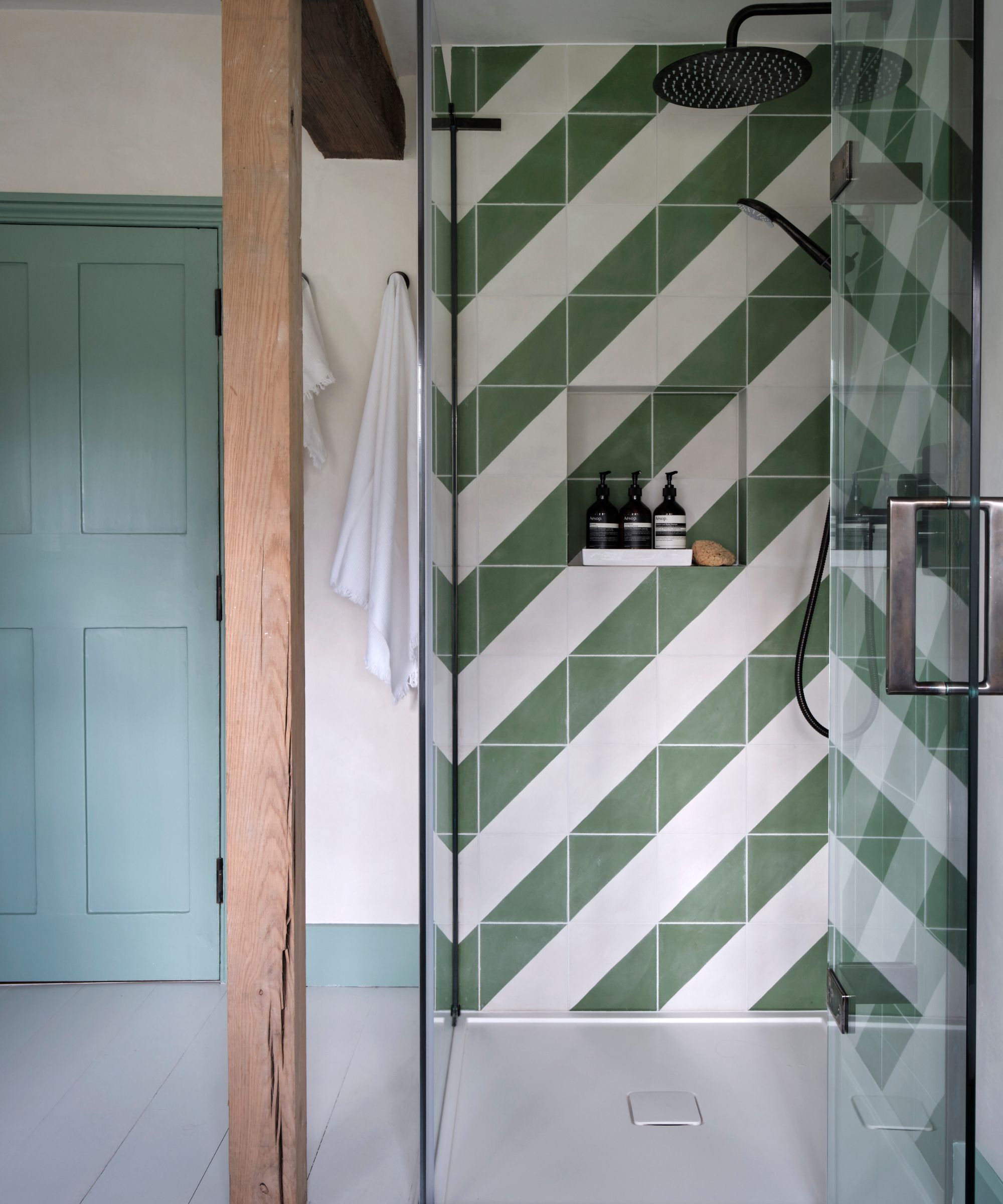 Bathroom with green and white tiled shower in stripe pattern and pale blue door